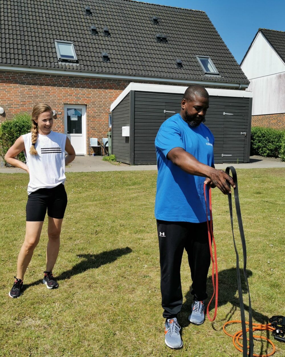 Personlig træner hjælper med træning på græsplæne foran kundes hjem